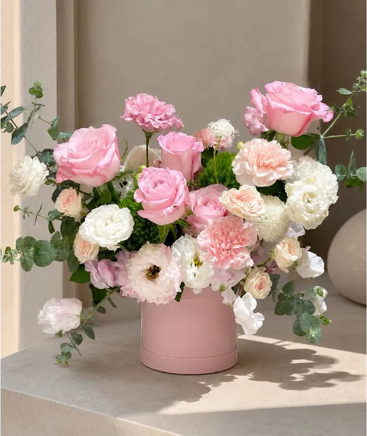 Caja floral rosa con rosas premium rosadas, mini rosas, claveles, lisianthus y flores blancas de temporada.