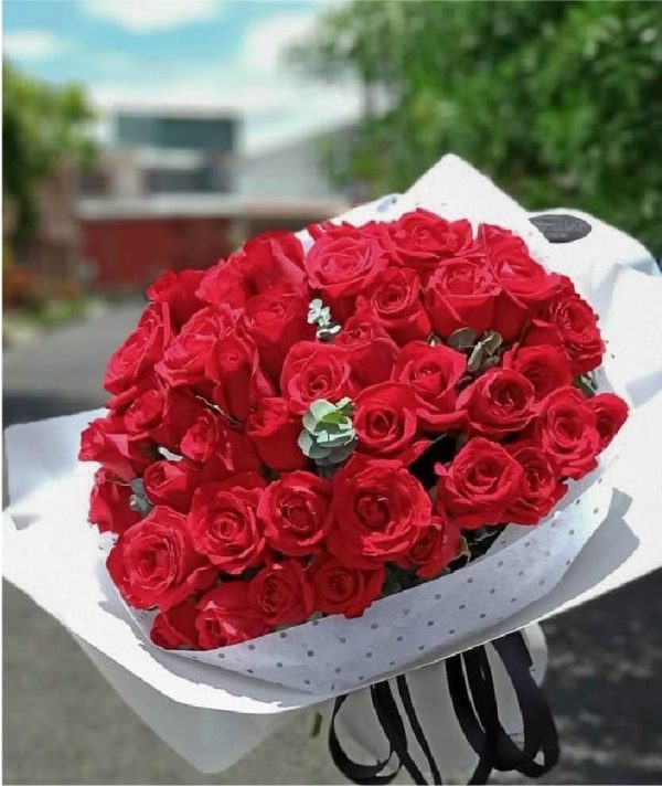 Ramo de rosas rojas premium envuelto en papel blanco con elegante listón negro.