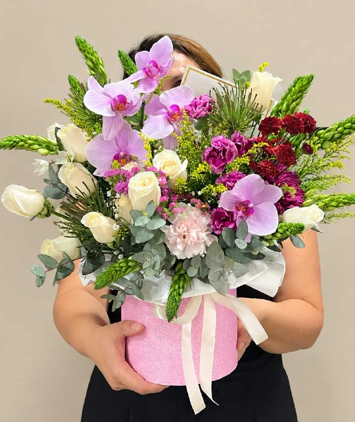 caja-floral-encanto-de-orquídeas-y-rosas Caja floral rosada con orquídeas Phalaenopsis, rosas blancas, claveles y eucalipto en tonos rosa, lila, blanco y vino.